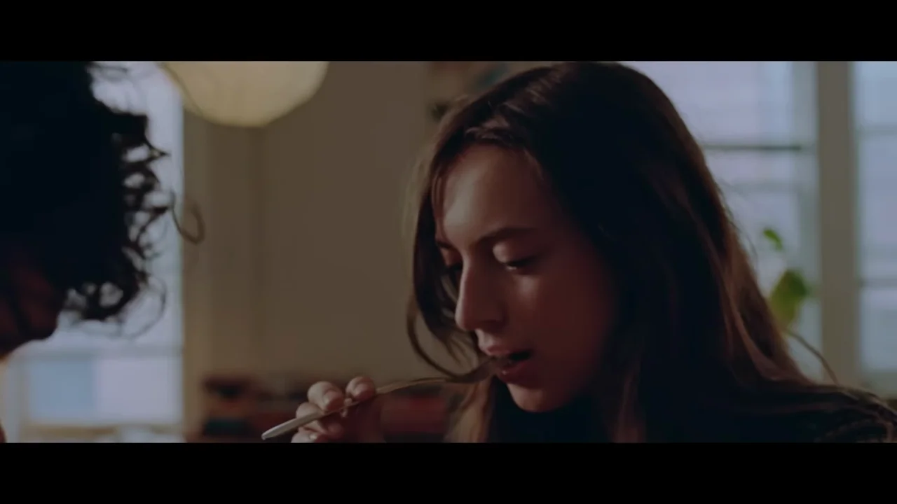 A face and a tasting action introduce a quiet kitchen scene.
